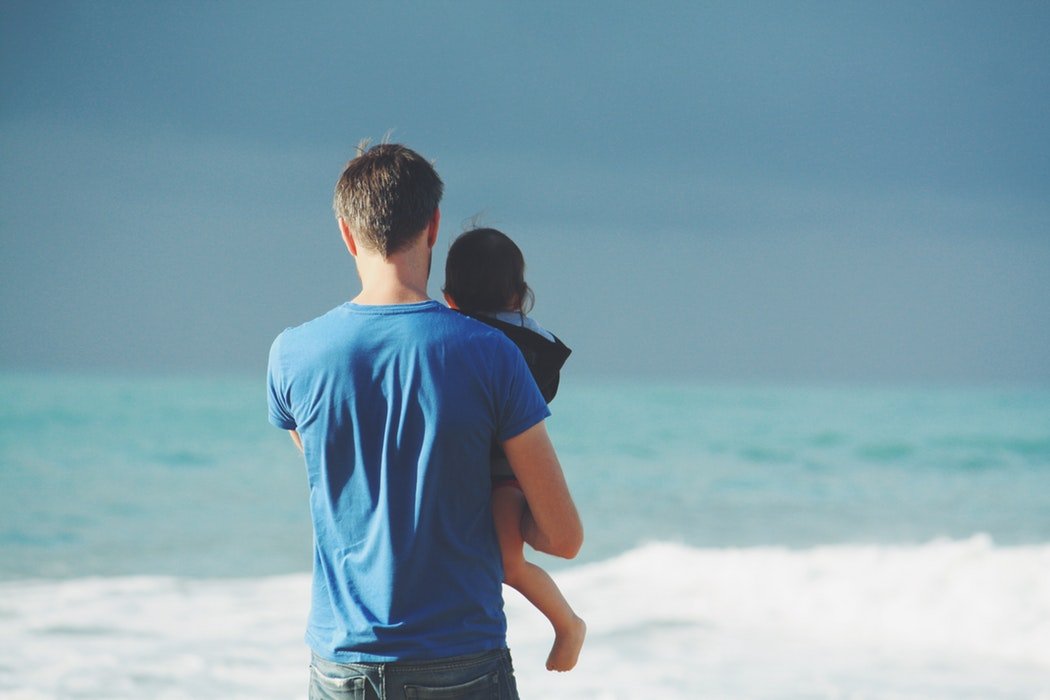 father holding his daughter in front of the ocean