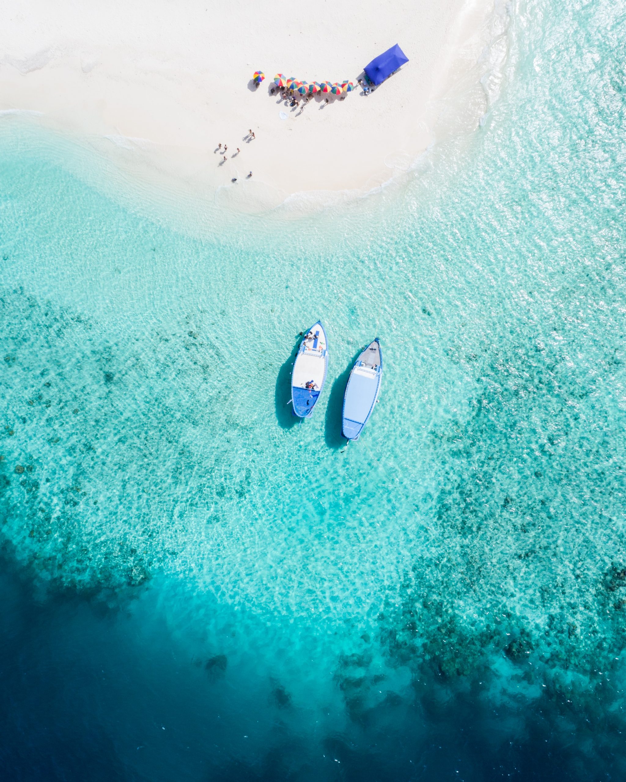 two boats in clear blue waters next to a beach